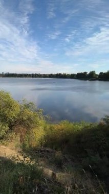 Gölün kenarında dikey video 4k. Nehir uçurumu. Mavi gökyüzü ve nehirdeki güzel su. Göl kenarında yürüyüş. Nehrin kıyısına yürü. Ukrayna.