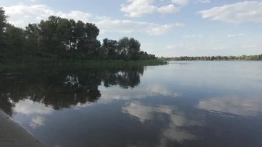 Su kıyısındaki doğal manzara. Göl kıyısı. Sudaki bulutların yansıması. Nehirle akşam manzarası. Denize doğru yürü. Su yüzeyi. Ukrayna. Düz renk profilli 4k video. D-Günlük M.