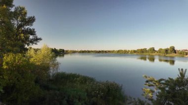 Altın güneş ışığı, bereketli sonbahar ağaçları tarafından çerçevelenmiş sakin bir nehri yıkıyor. Sakin suda yansımalar parıldıyor, bu sakin orman manzarasında huzur ve sükuneti davet ediyor..