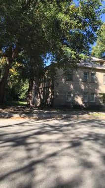  Uzun ağaçlarla gölgelenmiş iki katlı tuğladan bir evi olan sessiz bir yerleşim yeri. Güneş ışığı yaprakların arasından süzülür, yumuşak gölgeler bırakır. Klasik cazibe ve yeşillikle huzurlu bir şehir manzarası..