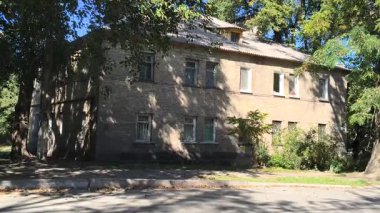  Uzun ağaçlarla gölgelenmiş iki katlı tuğladan bir evi olan sessiz bir yerleşim yeri. Güneş ışığı yaprakların arasından süzülür, yumuşak gölgeler bırakır. Klasik cazibe ve yeşillikle huzurlu bir şehir manzarası..