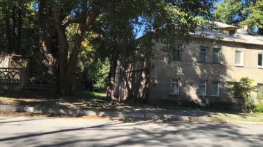  Uzun ağaçlarla gölgelenmiş iki katlı tuğladan bir evi olan sessiz bir yerleşim yeri. Güneş ışığı yaprakların arasından süzülür, yumuşak gölgeler bırakır. Klasik cazibe ve yeşillikle huzurlu bir şehir manzarası..