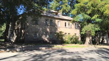  Uzun ağaçlarla gölgelenmiş iki katlı tuğladan bir evi olan sessiz bir yerleşim yeri. Güneş ışığı yaprakların arasından süzülür, yumuşak gölgeler bırakır. Klasik cazibe ve yeşillikle huzurlu bir şehir manzarası..