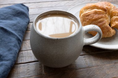 Bir fincan sıcak kahve ve bir kruvasan yakın çekim. Sıcak, davetkar bir sahne. Rahatlık ve rahatlık için mükemmel...