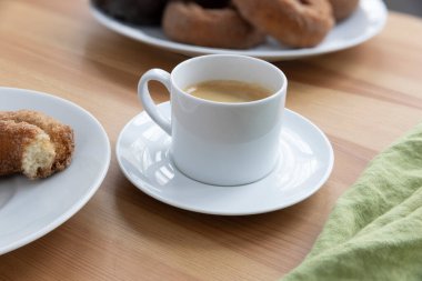 Arka planda donutlar olan beyaz bir fincan espresso getir..