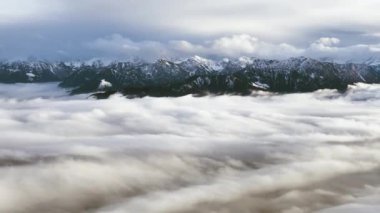 İsviçre 'deki bulutlu ve sisli İsviçre Alpleri' nin günbatımında tepelerde karlı havadan çekilmiş görüntüleri.