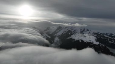 İsviçre 'deki bulutlu ve sisli İsviçre Alpleri' nin günbatımında tepelerde karlı havadan çekilmiş görüntüleri.