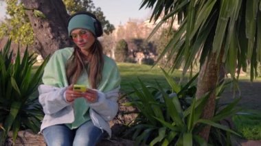 A girl in headphones listens to music in the park. High quality 4k footage