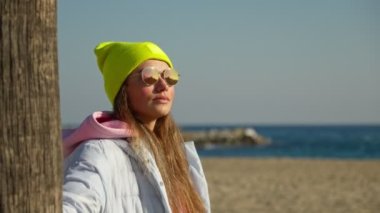 A girl in glasses near a palm tree and looks at the sea. The camera is in motion.
