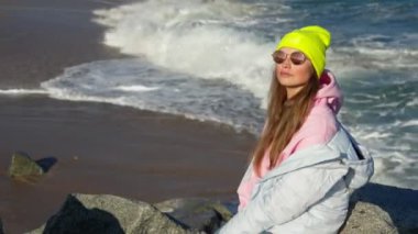 The girl sits on the rocks overlooking the sea. bright hat and sunglasses.