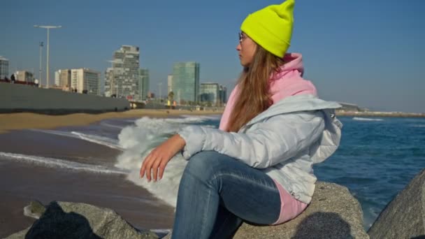 Дівчина Сидить Скелях Березі Моря Яскравий Капелюх Синя Куртка — стокове відео