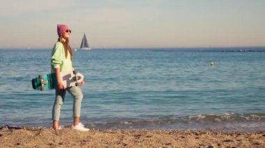 A young girl walks with a skate along the sea. High quality 4k footage