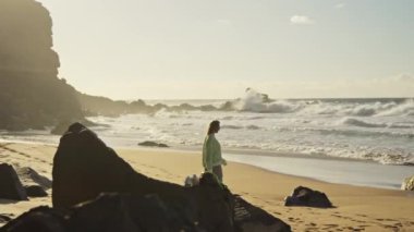 Kız dalgaların, azgın okyanusun ve günbatımının arka planında yürüyor. Yüksek kalite 4k görüntü