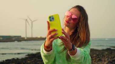Kız rüzgar türbinlerinin arka planında selfie çekiyor. Yüksek kalite 4k görüntü