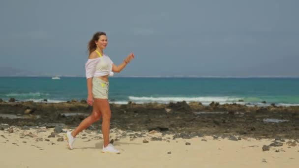 短いショートパンツを着た白いTシャツの女の子が海岸沿いを歩いている 高品質4K映像 — ストック動画