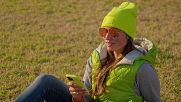 Девушка Смеется Глядя Свой Телефон Фоне Травы Высококачественные Кадры — стоковое видео