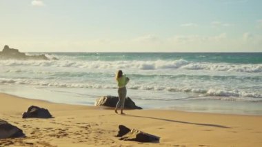 Kız dalgaların, azgın okyanusun ve günbatımının arka planında yürüyor. Yüksek kalite 4k görüntü