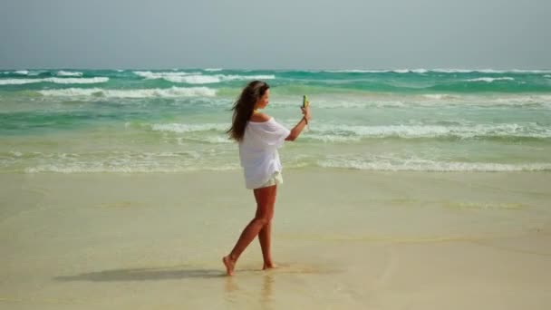 一个女孩在美丽的海滩上自拍 拿着智能手机摆姿势 高质量的4K镜头 — 图库视频影像