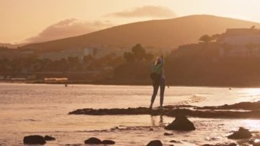  Gün batımında deniz kıyısında zarif bir şekilde dans eden bir kızı seyredin. Arka planda dalgalar yavaşça çarpıyor. Yüksek kalite 4k görüntü