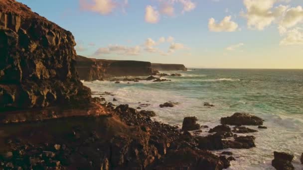 在崎岖的岩层附近航行 目睹汹涌的海浪冲击着岩石的背景 炽热的落日以其迷人的色彩描绘着天空 — 图库视频影像
