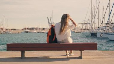 Turist bir kız, hareketli bir yat kulübündeki bir bankta dinlenirken rahatlama ve keyif alır. Yüksek kalite 4k görüntü
