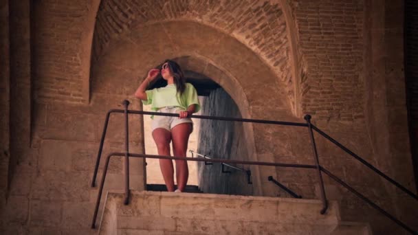 少女は要塞の階段を優雅に登り 歴史的な壁を通ってエコーをかけます 各ステップは要塞の豊かな歴史と建築の素晴らしさを明らかにします — ストック動画