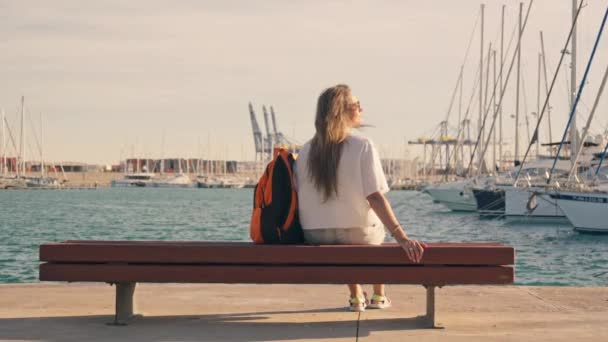 Κορίτσι Κάθεται Ένα Παγκάκι Στη Μαρίνα Της Θάλασσας Γιοτ Υψηλής — Αρχείο Βίντεο