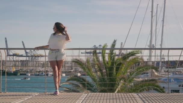 鮮やかな海のマリーナを背景に立っている少女の美しさを賞賛し 強い風が優雅に吹く 高品質4K映像 — ストック動画
