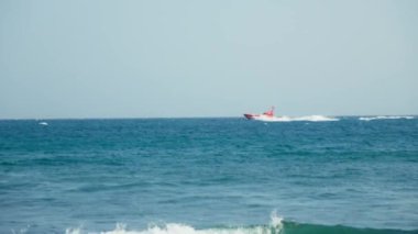Kırmızı bir sürat teknesi, arkasında beyaz bir köpük izi bırakarak dalgaların arasında hızla ve enerjisiyle hızla ilerler.
