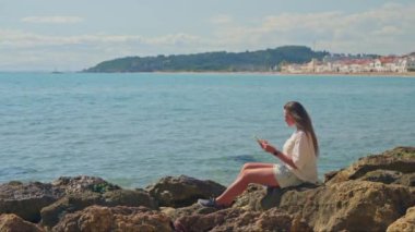 Okyanusun yanındaki bir kayanın üzerinde oturan bir kadın.