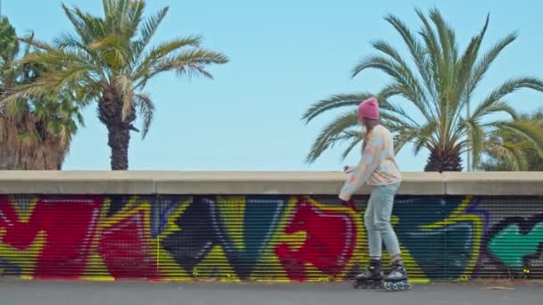 グラフィティで覆われた壁の隣にスケートボードに乗っている男 — ストック動画