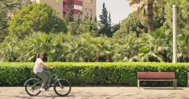 公園のベンチを通り過ぎて自転車に乗っている女性 高品質の4K映像 — ストック動画