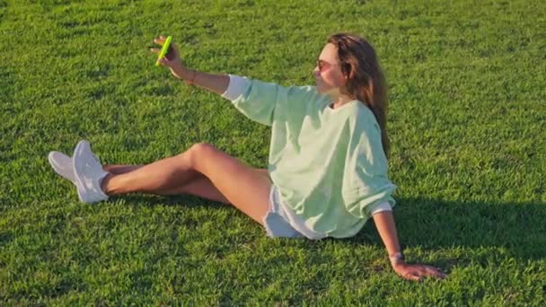 女の子は草の上に座っているセルフィーを取る 高品質の4K映像 — ストック動画