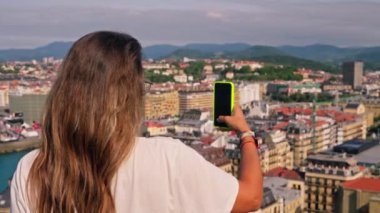 Kadın cep telefonuyla şehir görüntülerini yakalıyor.