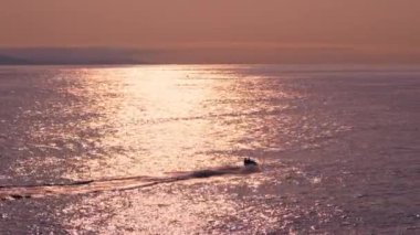 Bir jet ski rengarenk bir günbatımı gökyüzünün altında bir su kütlesinin üzerinde hızla ilerliyor..