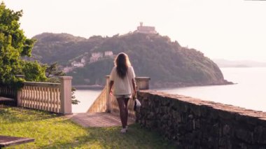 Taş bir duvarda duran bir kadın, bir su kütlesine bakıyor..