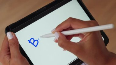 Bir birey bir tablet ekranda bir kalem kullanarak yazıyor.