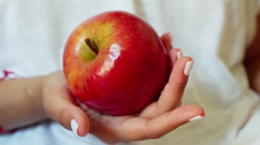 Elinde olgun kırmızı bir elma tutan bir kadın meyveyi yakından gösteriyor..