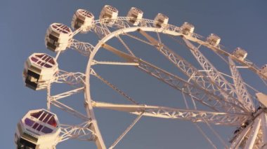 Büyük bir dönme dolap, açık mavi gökyüzüne karşı dimdik durur. Renkli kulübelerini ve karmaşık iskeletini gösterir..