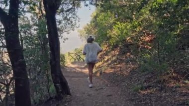 Ağaçlar ve yeşilliklerle çevrili bir orman yolunda yürüyen bir insan..