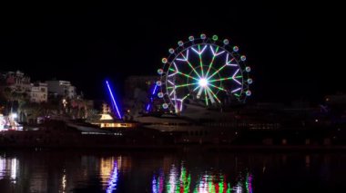 Parlak bir dönme dolap karanlık gece gökyüzüne karşı dimdik ayakta duruyor, göz kamaştırıcı bir manzara sunuyor..