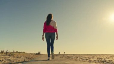 Pembe gömlekli bir kadın tahta bir kaldırımda geziniyor..