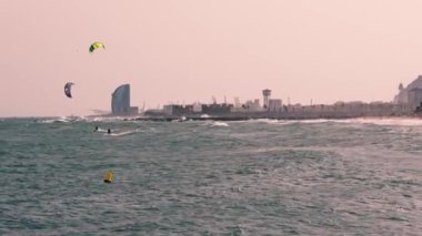 Bir grup insan bir su kütlesinin üzerinde uçurtma sörfü yapıyor, sporun heyecanını yaşıyorlar..