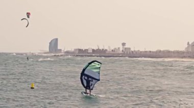 Arka planda şehir silüeti olan bir rüzgâr sörfçüsü..