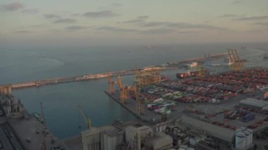 Gün batımında vinçler ve konteynırlarla bir limanın havadan görüntüsü..