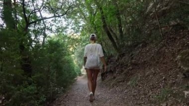 Ağaçlarla çevrili bir orman yolunda gezinen bir kadın..