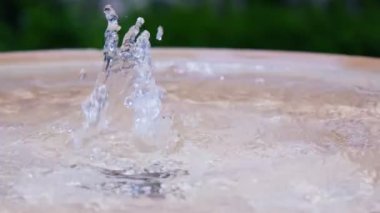 Su damlacıkları yemyeşil bir bahçedeki dairesel bir çeşmenin yüzeyinden fışkırarak gün boyunca dingin ve ferahlatıcı bir atmosfer yaratırlar..