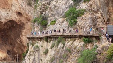 Turist grupları kayalık bir uçurum kenarındaki ahşap bir geçidi keşfederek, güneşli bir açık havada kanyonun nefes kesici manzarasının tadını çıkarıyorlar..