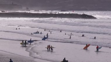 Sörfçüler ve plaja gidenler güneş batarken kıyıda toplanır, dalgalara biner ve kıyı sahilinin canlı atmosferinin tadını çıkarırlar..