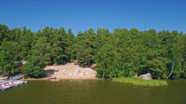 Güneş banyosu yapanlar göl kenarında sakin bir günün tadını çıkarırlar, yemyeşil ağaçlar ve açık gökyüzüyle çevrili, günlük hayattan mükemmel bir kaçış yaratırlar..